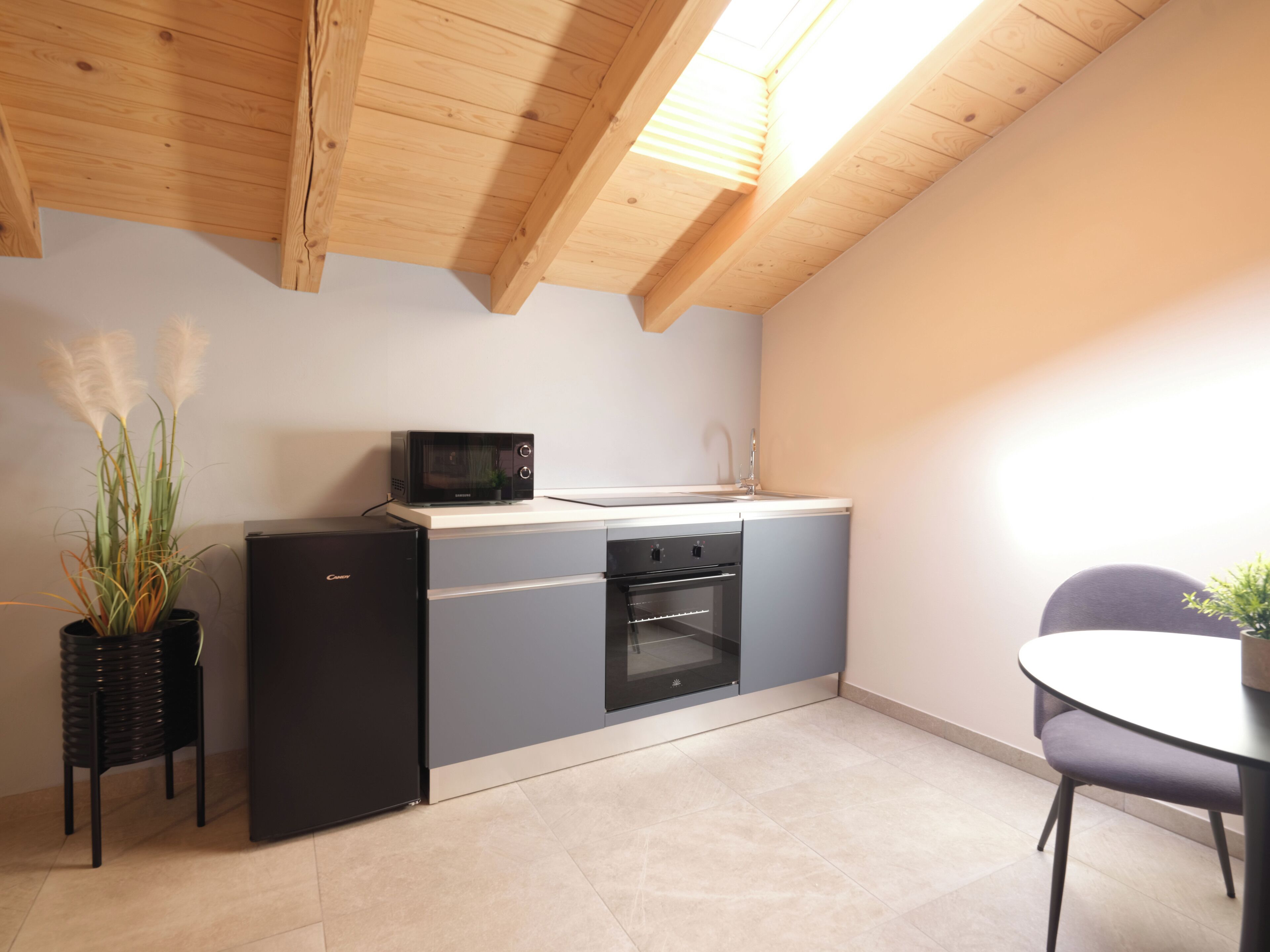 A compact kitchen with a microwave, oven, and sink, a small dining table, and a potted plant.