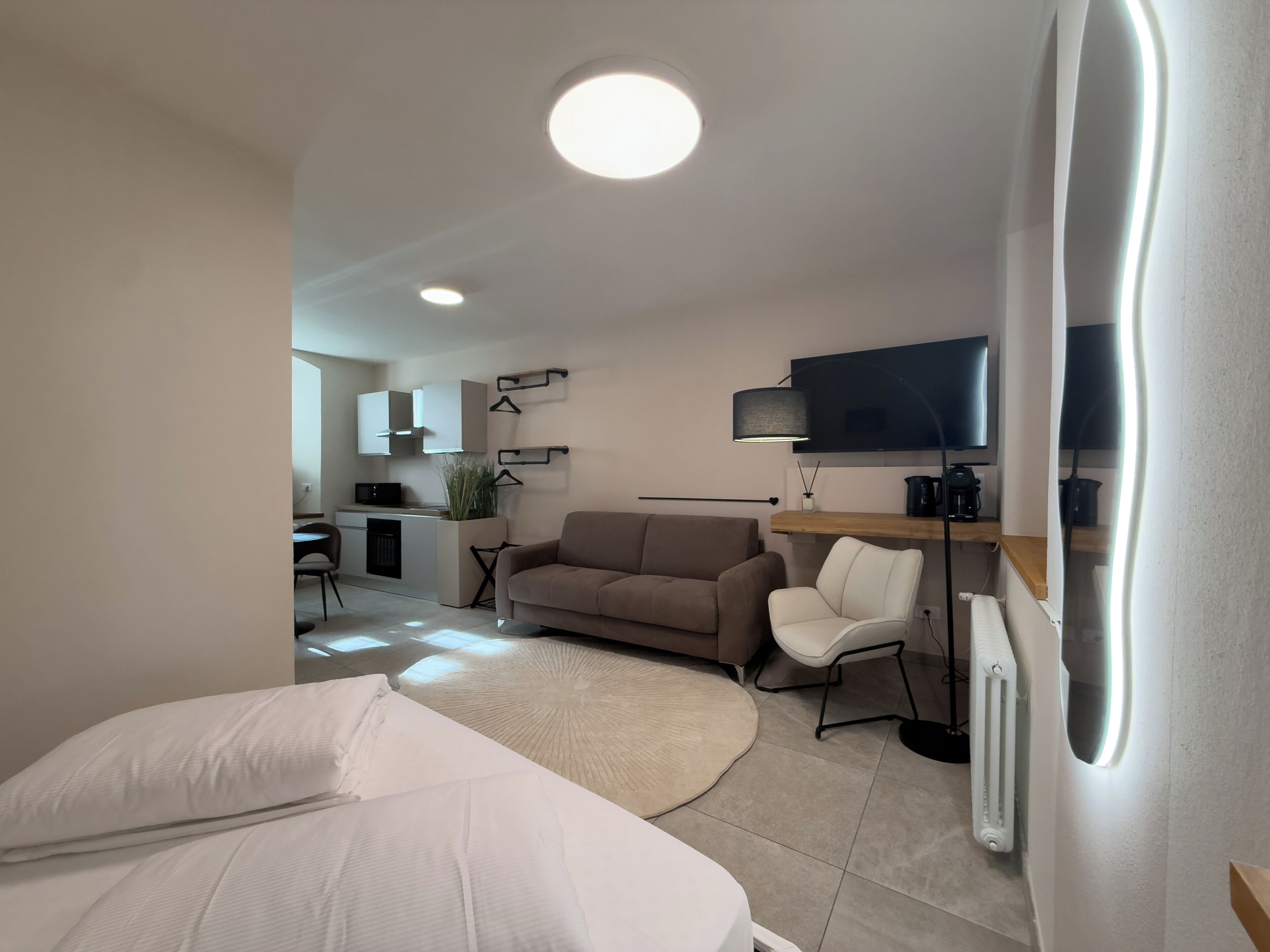 Una sala moderna con un sofá, una silla, un televisor y una cocina al fondo.