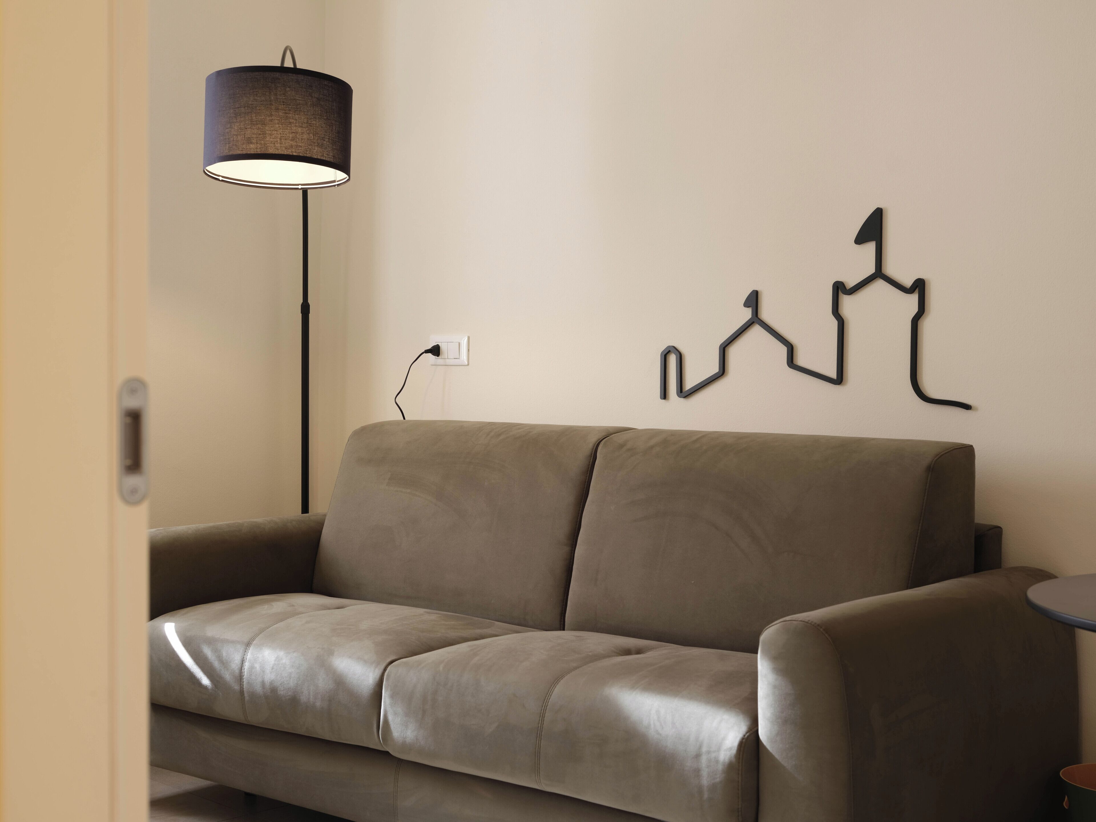 Een moderne woonkamer met een leren bank, een vloerlamp en een abstract kunstwerk aan de muur.