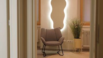 Une pièce avec un fauteuil moderne, un luminaire fixé au mur et une plante en pot.