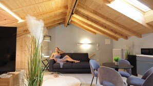 A modern loft with a wooden ceiling, a sofa, a dining table, chairs, a TV, and a kitchen area. - Soul of Trento Vicolo Maddalena (Trento)
