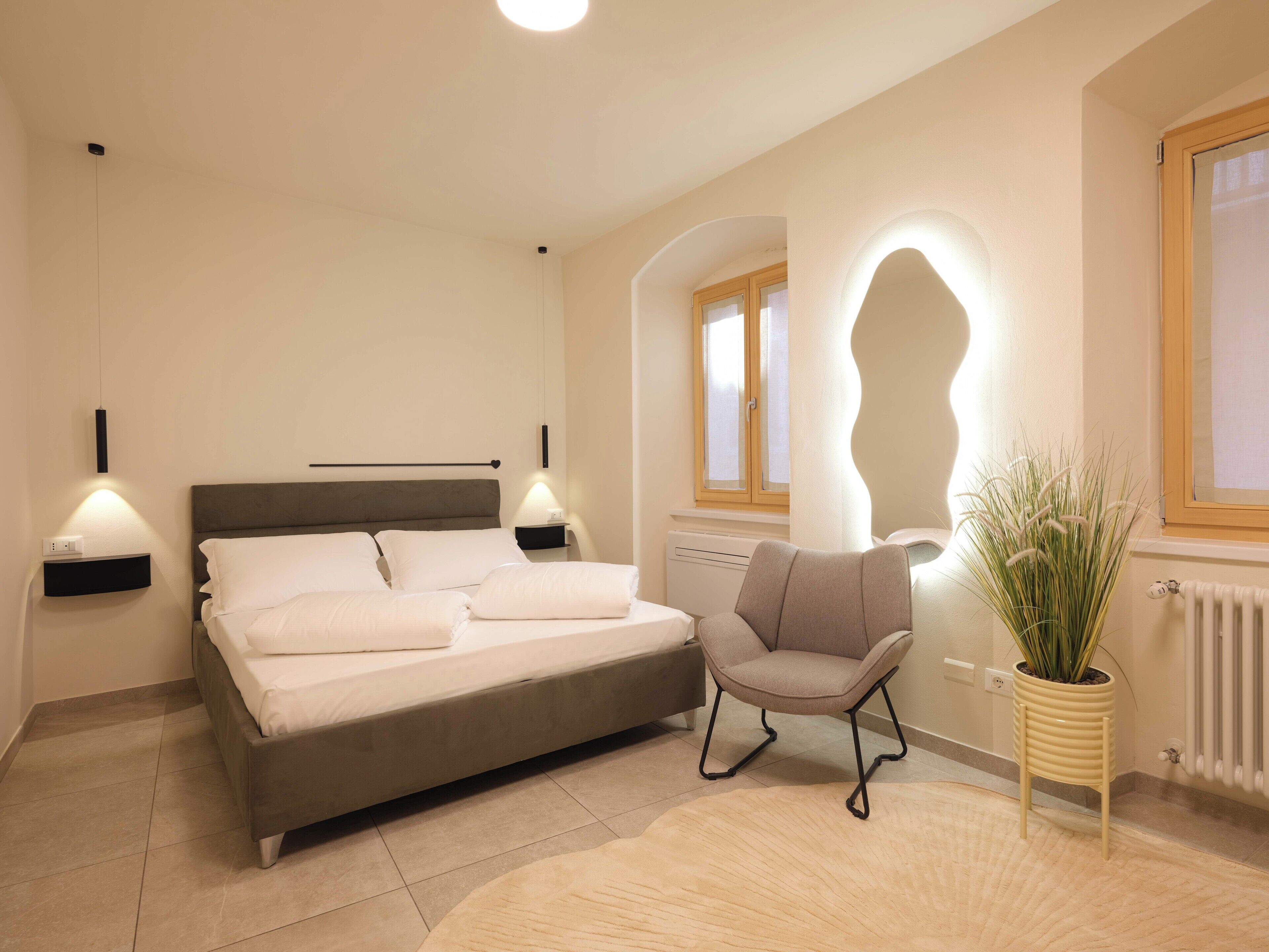 Un dormitorio con cama, mesitas de noche, una silla, un radiador y una ventana.