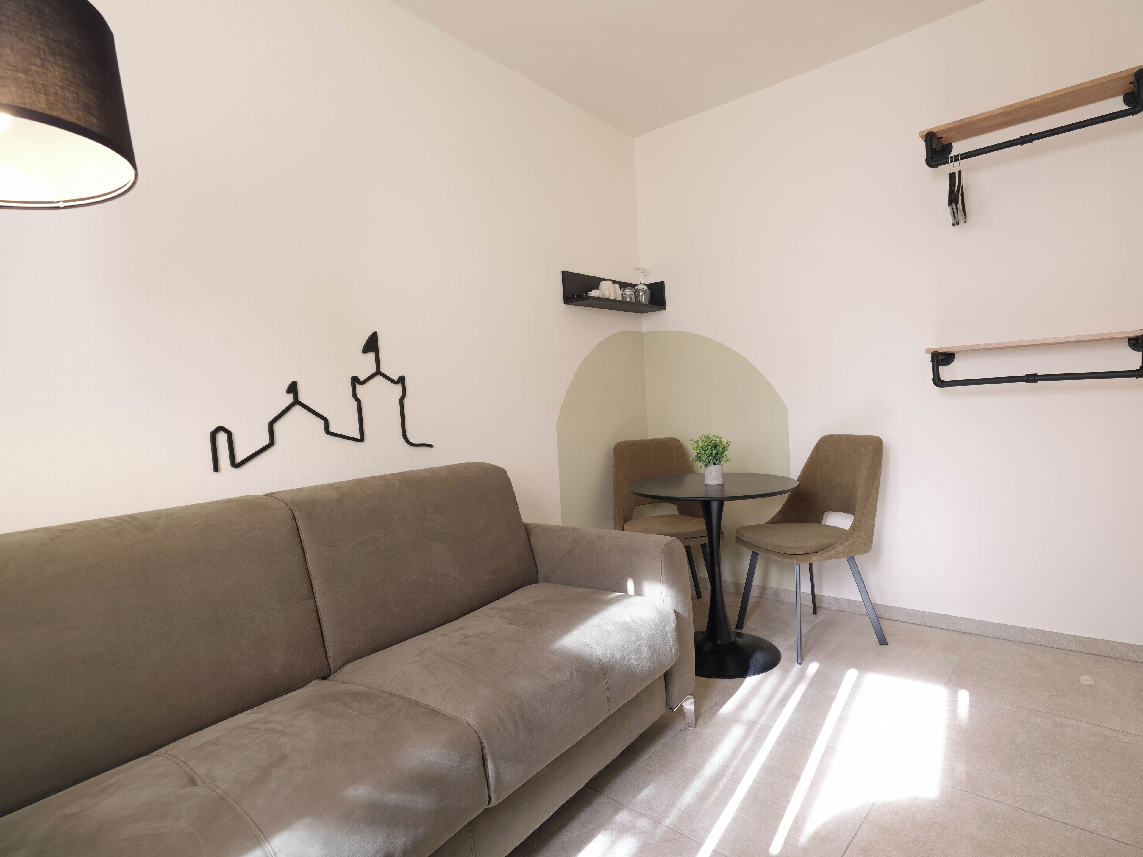 Ein modernes Wohnzimmer mit einer Couch, Sesseln, einem kleinen Tisch mit einer Pflanze und minimalistischer Einrichtung.