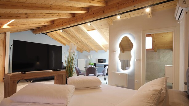 A modern bedroom with a large bed, a flat-screen TV, and a wooden ceiling. - Soul of Trento Vicolo Maddalena (Trento)