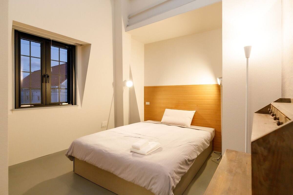 A hotel room with a bed, a window, a headboard, a bedside table, and a staircase.
