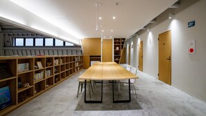A library with a long table, bookshelves, and a ceiling light.