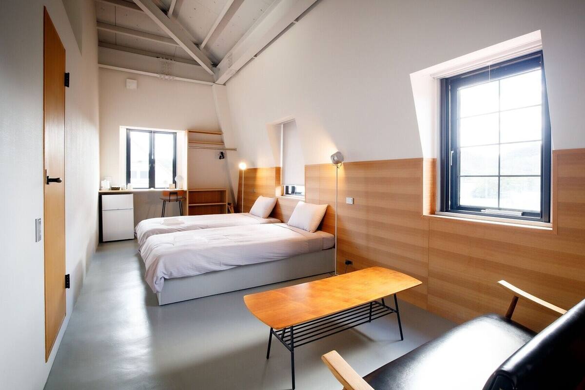 A modern, well-lit room with a bed, bedside table, and a small desk area.