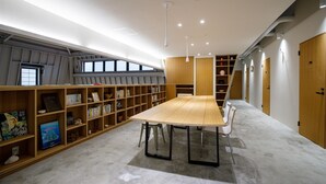 A library with a long wooden table, bookshelves, and a staircase.