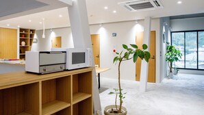 A modern room with a wooden desk, two white appliances, a potted plant, and a large window.