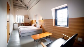A modern, well-lit room with a bed, bedside table, and a small desk area.