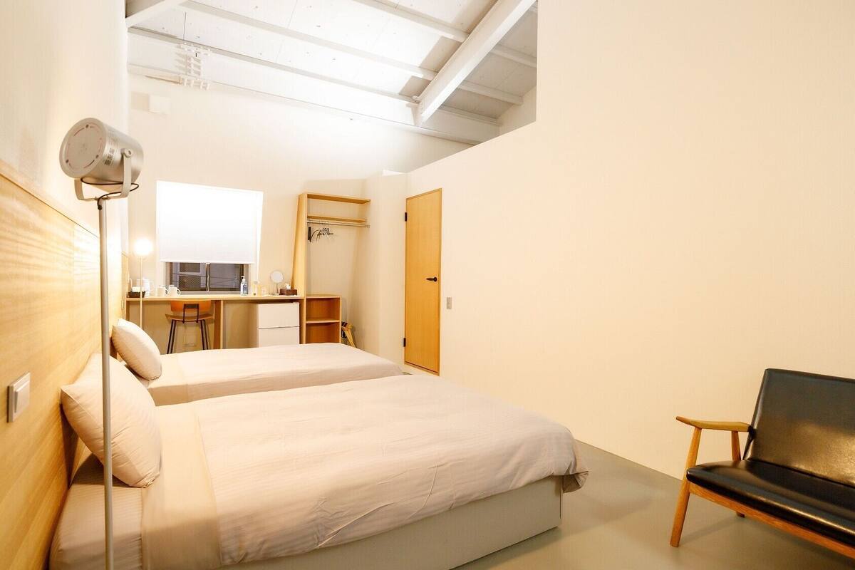 A room with two beds, a desk, a chair, a wardrobe, and a ceiling fan.