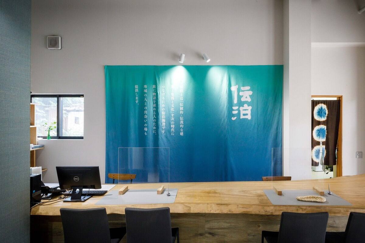 A conference room with a large table, chairs, a computer, and a wall with Japanese text.