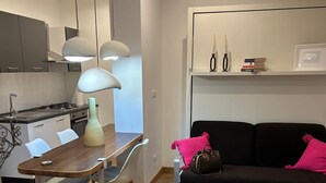 Eine moderne Küche mit Esstisch und Stühlen, eine schwarze Couch mit rosafarbenen Kissen und ein Bücherregal mit Büchern und Dekoration.