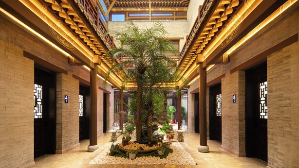 Um lobby de hotel com uma palmeira central, vigas de madeira no teto e designs de portas tradicionais chinesas.