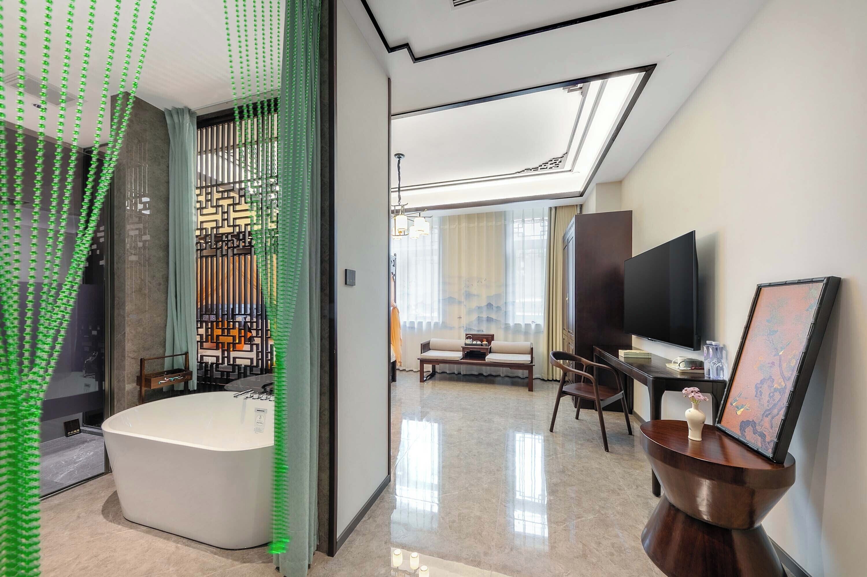 Quarto de hotel moderno com uma banheira grande, televisão de tela plana, sofá e área de refeições.
