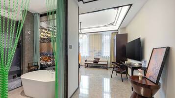 Quarto de hotel moderno com uma banheira grande, televisão de tela plana, sofá e área de refeições.