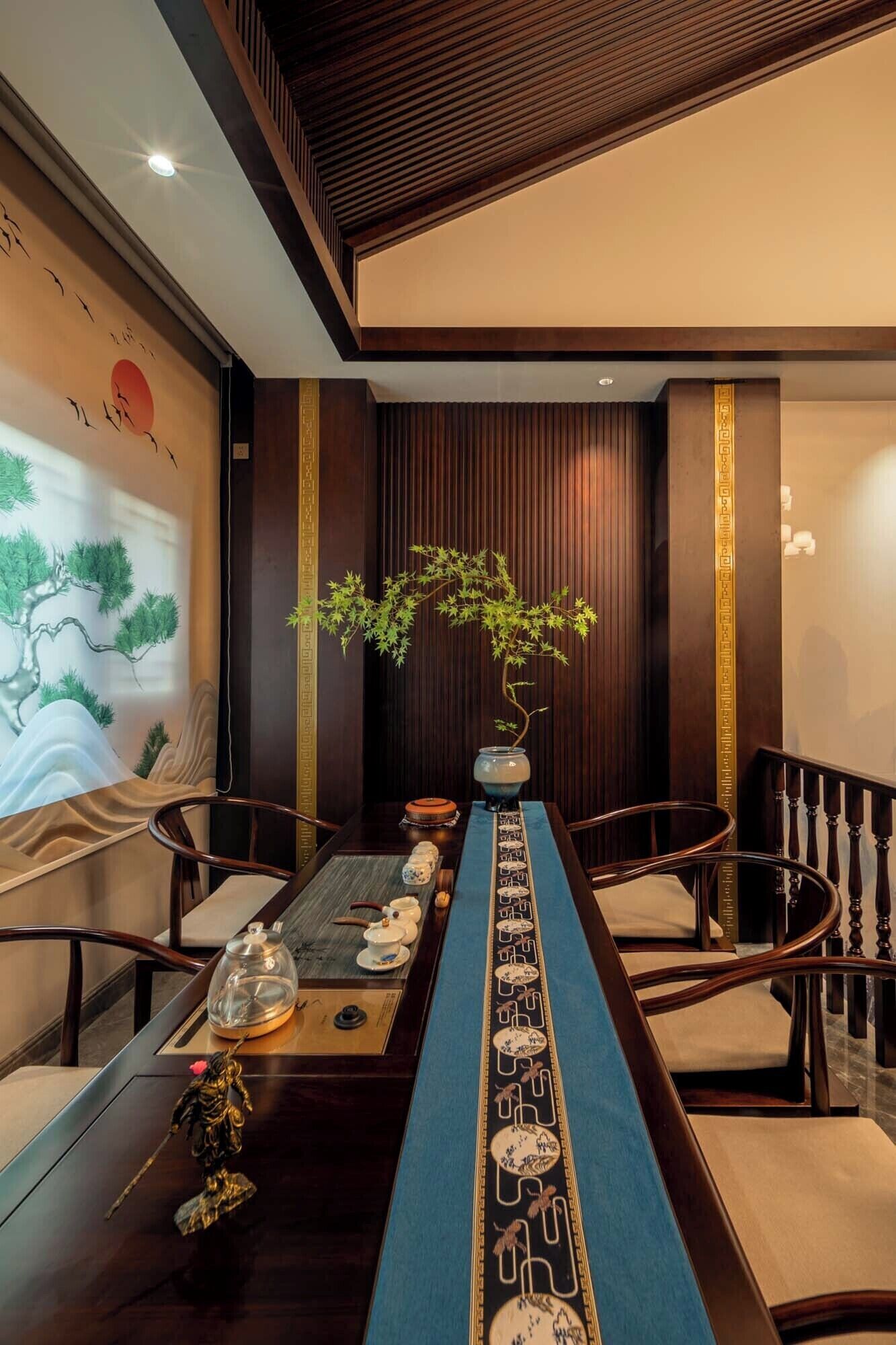 A traditional-style dining area with a long table, chairs, a bonsai tree centerpiece, and a decorative wall with artwork.