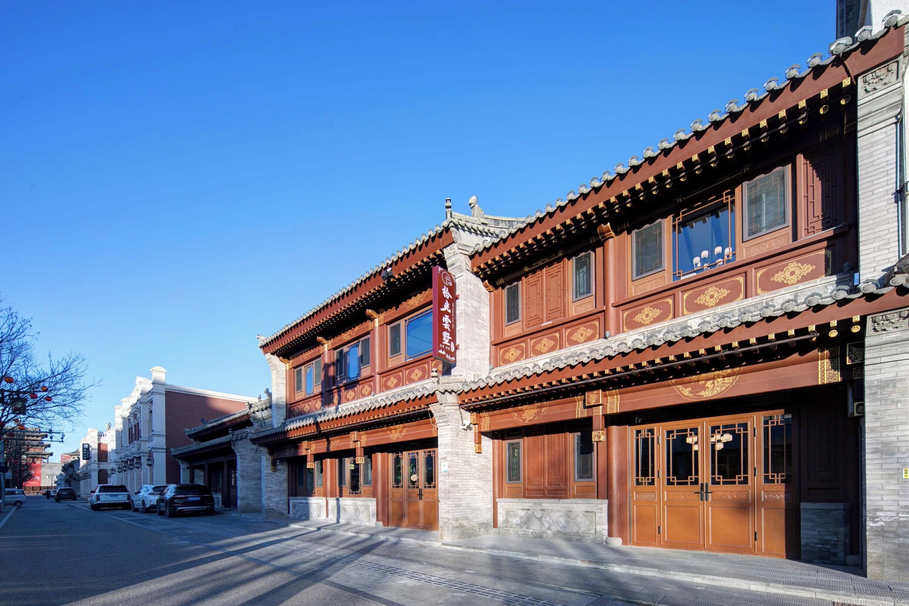 Un edificio tradicional con puertas y ventanas de madera, cielo azul despejado y una calle con coches estacionados.