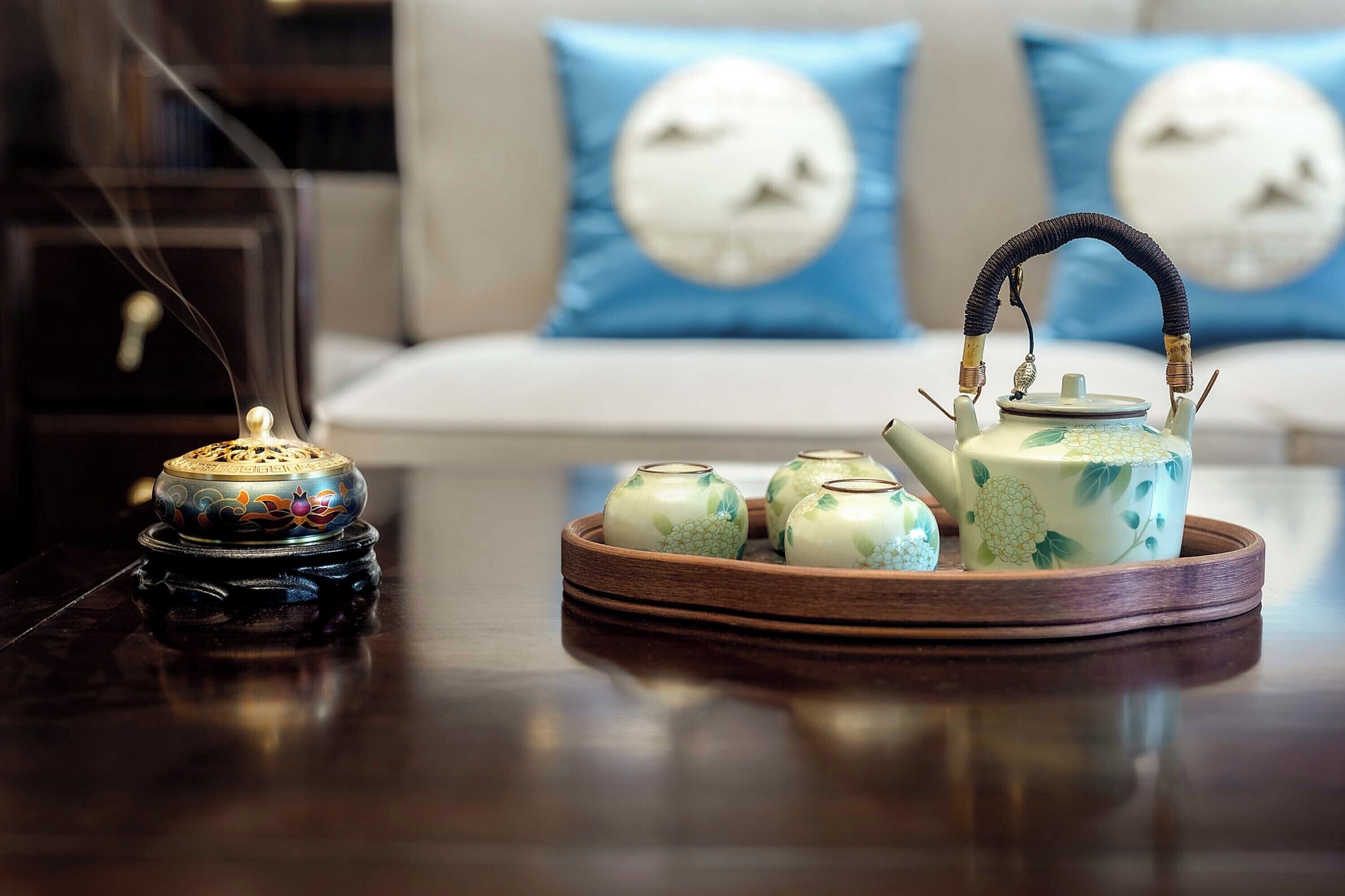 A tea set on a tray with a teapot and cups, a decorative jar, and a small incense burner on a table.