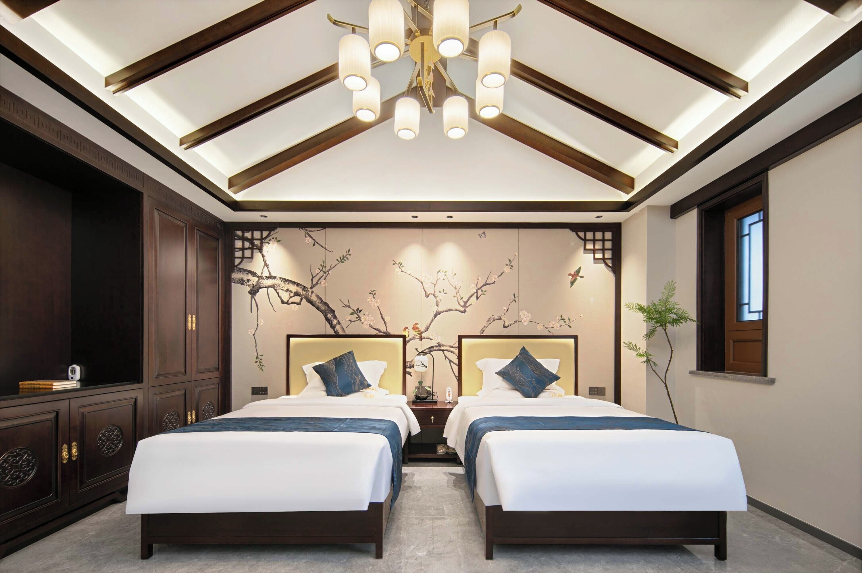 A hotel room with two beds, a large chandelier, a wall mural, and a window.