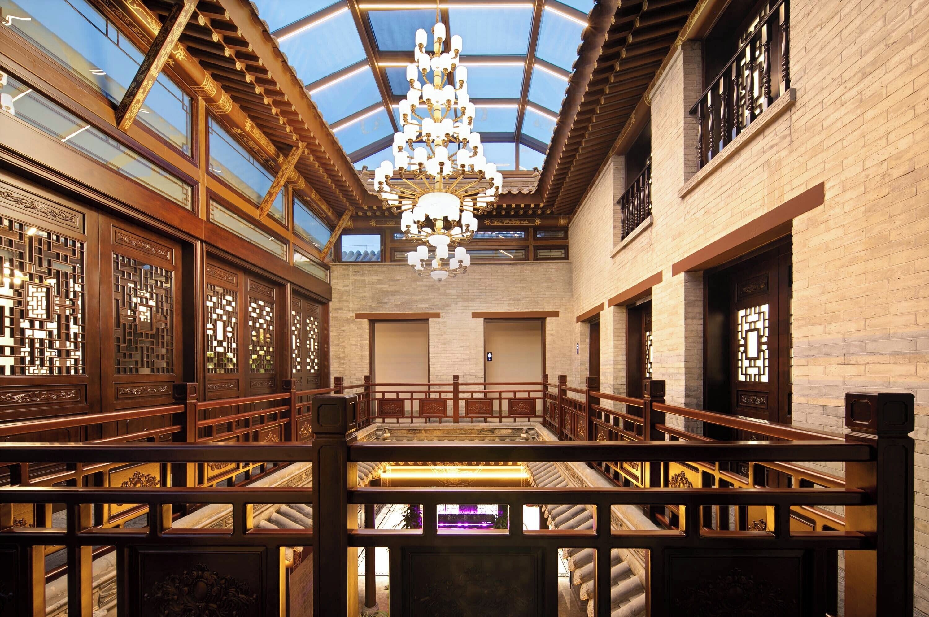 A spacious atrium with a high ceiling, wooden railings, and a central chandelier.