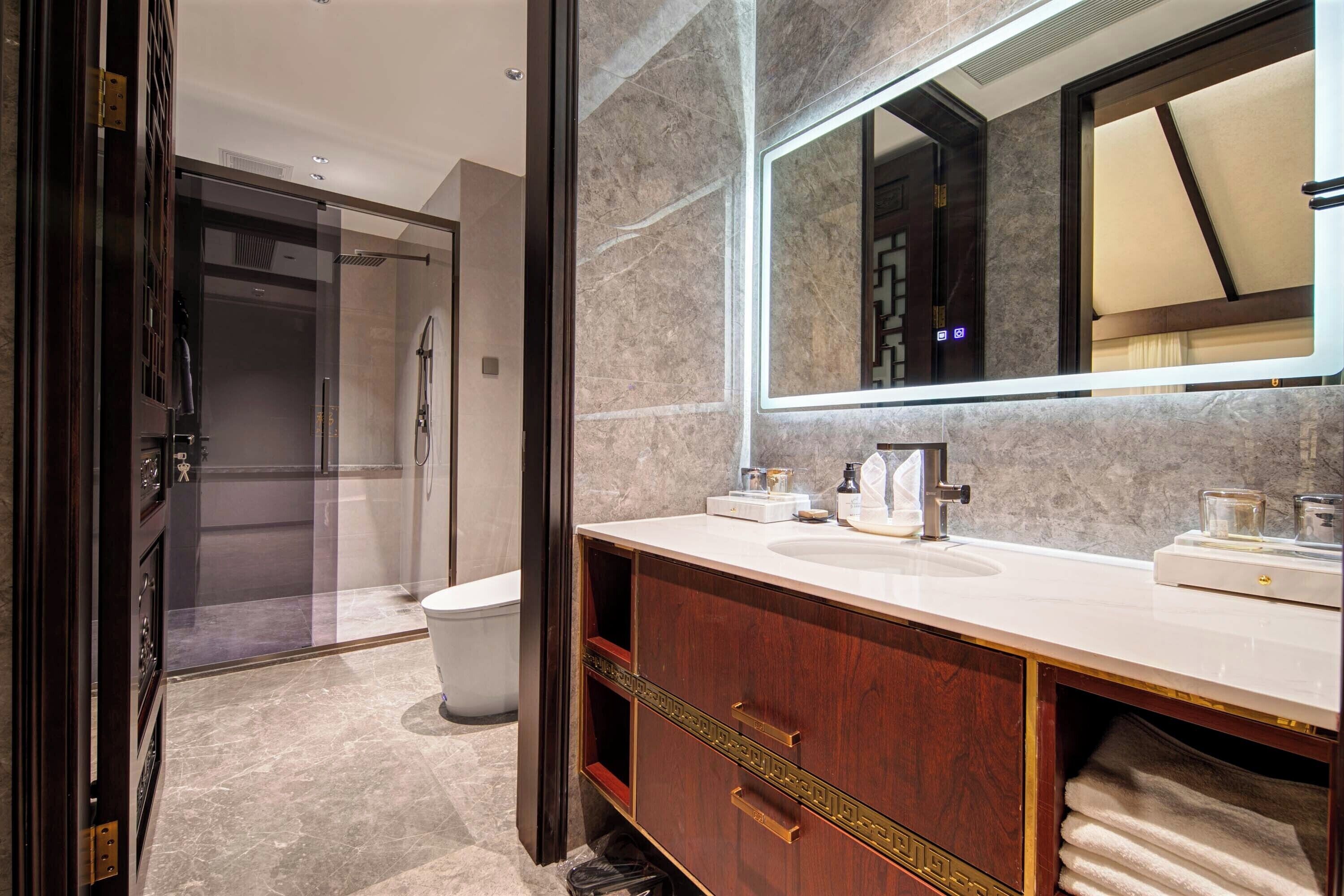 A modern bathroom with a marble wall, a large mirror, a sink, and a vanity with drawers.