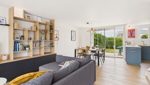 Ein modernes Wohnzimmer mit einem grauen Sofa, Holzregalen und einem Essbereich mit Tisch und Stühlen.