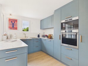 A modern kitchen with light blue cabinets, a white countertop, and a built-in oven. - Sea view for 6 with garden, 150m from the beach (Arzon)