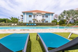 Un bâtiment à deux étages doté d’une piscine, de chaises longues et d’une pelouse bien entretenue.