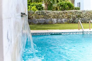 A swimming pool with a water feature, surrounded by a landscaped garden and a stone wall. - Luxury New 2BR Apartment near Blue Bay Beach, 20m Pool, Sleeps max 4 (Sint Michiel)