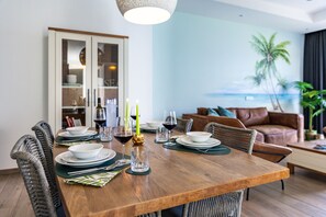Un coin repas avec une table en bois dressée pour quatre personnes, une vue sur l’océan, et un salon avec un canapé en cuir.