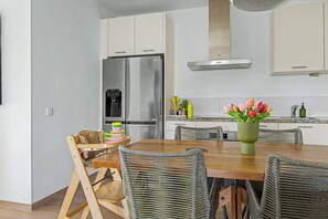 A modern kitchen with a stainless steel refrigerator, a built-in oven, and a range hood. There is a dining table with chairs and a vase of flowers. - Luxury New 2BR Apartment near Blue Bay Beach, 20m Pool, Sleeps max 4 (Sint Michiel)