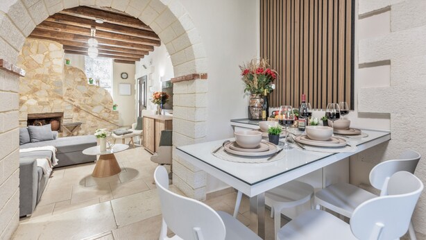 Une cuisine moderne avec une arche en pierre, une table à manger entourée de chaises blanches et un plafond en bois.