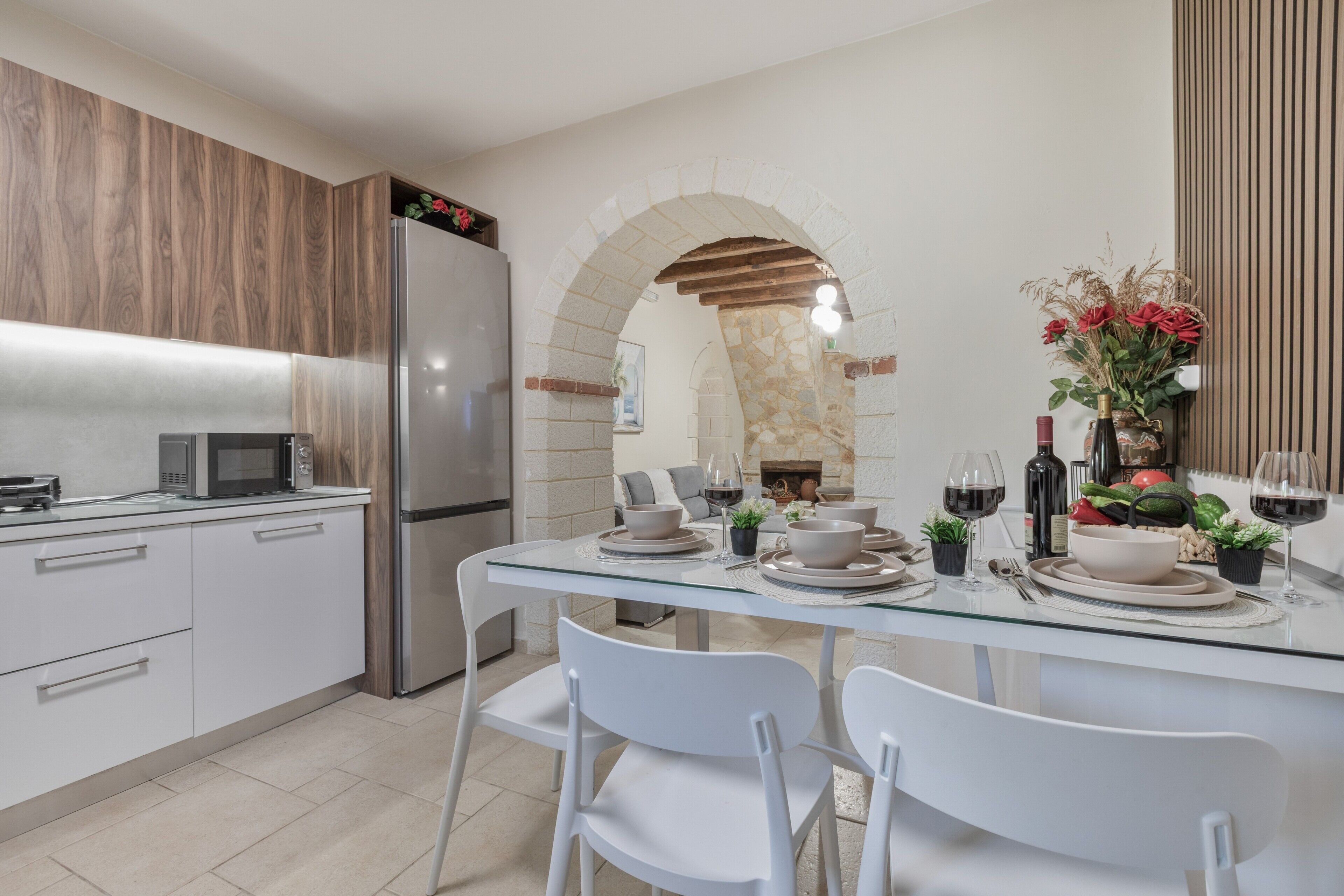 Una cocina moderna con mesa de comedor de vidrio, sillas blancas, un arco de piedra y un refrigerador empotrado.
