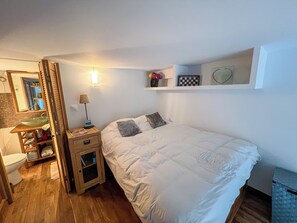 A bedroom with a bed, bedside table, lamp, mirror, and a shelf with decorative items. - Studio in belle époque villa in the golden triangle (Beaulieu-sur-Mer)