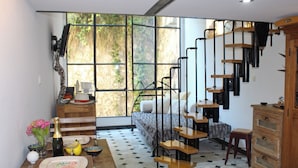 Une pièce comprenant un lit, une table à manger ornée d’un vase de fleurs, un escalier et une fenêtre donnant sur un paysage verdoyant.