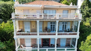 Un immeuble à plusieurs étages, doté de balcons, d’un mur en pierre et d’une végétation luxuriante.
