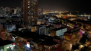 Paisagem urbana noturna com edifícios altos, um cruzamento movimentado e um posto de gasolina.