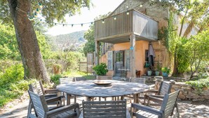 An outdoor dining area with a round wooden table and chairs, surrounded by stone walls and potted plants.