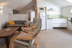 A compact living space with a sofa, a wooden dining table, a wooden chair, a kitchen area with a refrigerator, and a microwave.