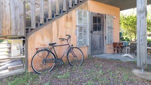 A wooden staircase leading to a building with a door and window shutters. A bicycle is parked against the building.