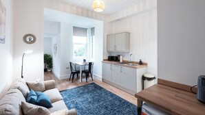 Uma sala de estar moderna com sofá, mesa de centro e área de jantar com mesa e cadeiras. Há também uma cozinha com armários e pia.
