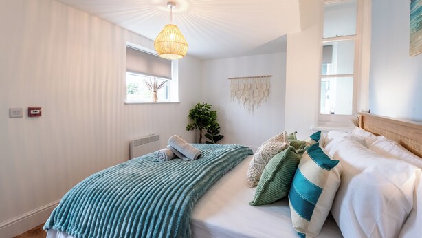 Quarto com cama, luminária pendente, janela e um painel de macramê na parede.