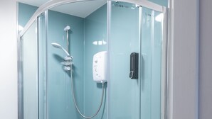 Área de chuveiro com paredes de vidro, chuveiro manual, painel de controle na parede e porta-papel higiênico.