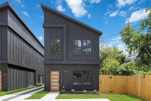 Une maison moderne à deux étages, dotée d’une façade sombre, d’un portail de garage bien visible et d’un jardin avant bien entretenu.