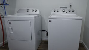 Kaksi valkoista Whirlpool-merkkiä olevaa kuivausrumpua on asetettu vierekkäin pyykinhuoneeseen, jossa on puulattia ja näkyvissä oleva pistorasia.