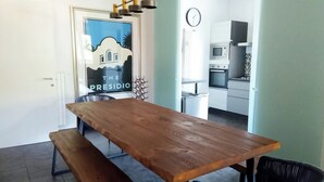 Un comedor con una mesa y banco de madera, un reloj en la pared y una cocina al fondo.