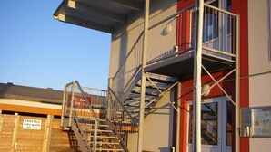 A building with a metal staircase leading to a red and white entrance, a sign indicating a bike parking point, and a door labeled 'Info Room.' - Nibelungenmotel (Poechlarn)