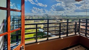 Un balcón con vista a un paisaje urbano, barandilla de metal y cielo despejado.