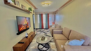Una sala de estar con televisor, sofá, mesa de centro y un estante en la pared con objetos decorativos.